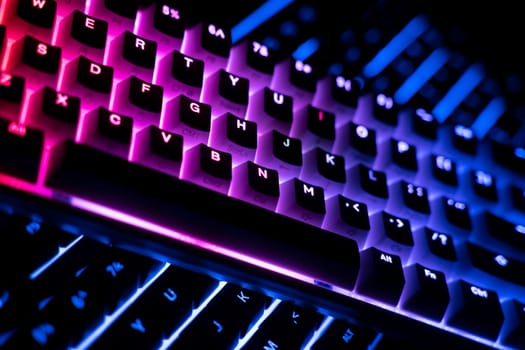 side view detail closeup of two illuminated mechanical gaming RGB keyboard on black desk on top of each other with keycaps lighting up in different colors in the dark