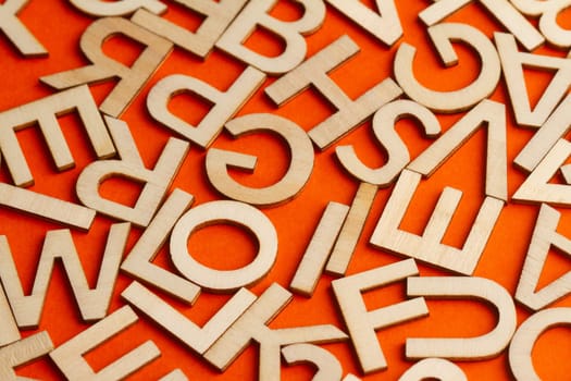 top view closeup detail macro of many wooden cut small alphabet letters on orange background