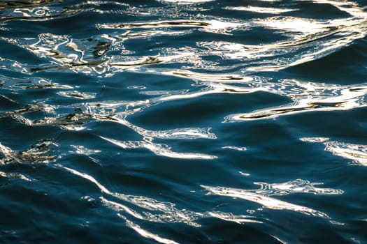 Dark blue rippled water surface background with bright golden sunlight reflection
