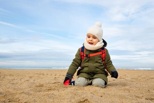 Little boy playing in the sand on beach in winter