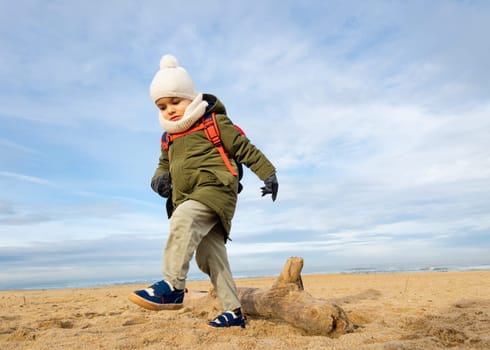 Little boy walking over a log on beach, winter season, low angle shot