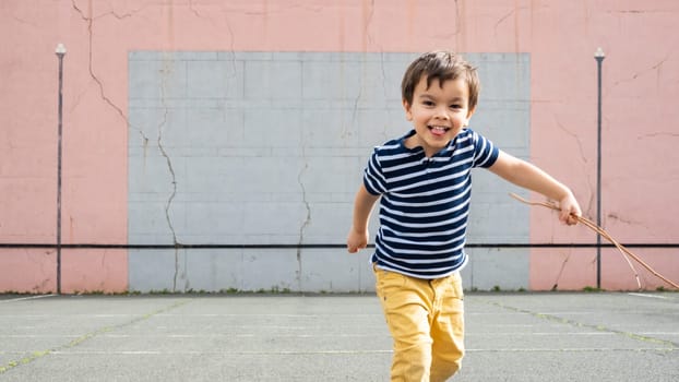Smiling little running towards camera on basque pelota court, toddler holding twigs in his left hand.