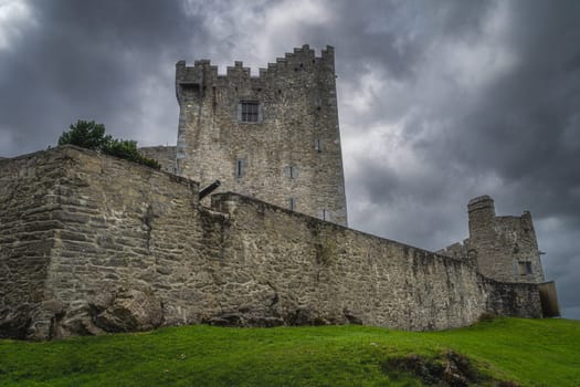 Cannon sticking out from fortification wall of 15th century Ross Castle with dramatic storm clouds in background, Ring of Kerry, Killarney, Ireland