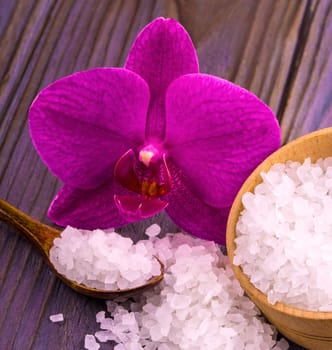 The White bath salt in a wooden cup with a spoon on a wooden table with an orchid
