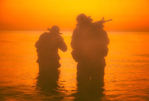 Commando soldiers walking in water, army special operations forces fighters sneaking in darkness, aiming assault rifles and observing shore during amphibious operation on coast at night or dawn
