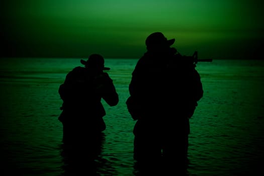 Two commando soldiers, army special operations fighters aiming assault rifles while coming out from water on shore at sunset or dawn. Coast guard shooters landing on sea coast, sneaking in water