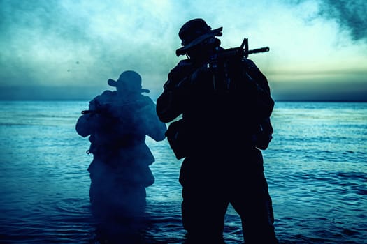 Commando soldiers walking in water, army special operations forces fighters sneaking in darkness, aiming assault rifles and observing shore during amphibious operation on coast at night or dawn
