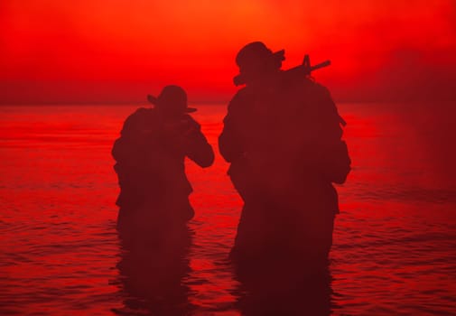 Commando soldiers walking in water, army special operations forces fighters sneaking in darkness, aiming assault rifles and observing shore during amphibious operation on coast at night or dawn