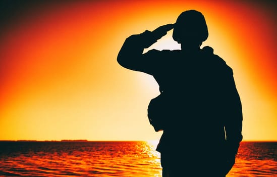 Silhouette of soldier in combat helmet and ammunition saluting on background of sunset sky. Army special forces fighter, Marines rifleman showing respect, greeting officer with salute gesture