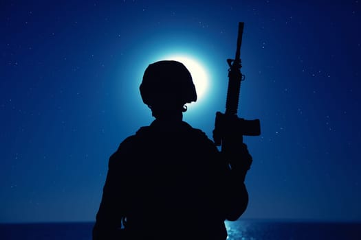 Silhouette of army soldier standing with service rifle in hand on background of night sky with moon. Armed Marines infantry in battle helmet and uniform ready for action, patrolling area in darkness