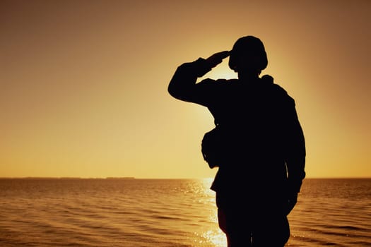 Silhouette of soldier in combat helmet and ammunition saluting on background of sunset sky. Army special forces fighter, Marines rifleman showing respect, greeting officer with salute gesture