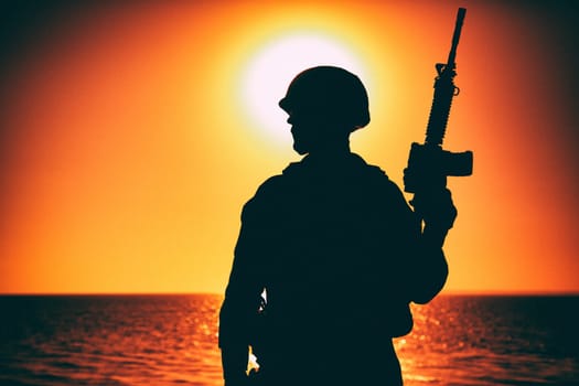 Silhouette of army soldier, special operations forces infantry rifleman, Marines fighter in combat helmet and ammunition standing with assault rifle in hand on background of sunset or dawn sky