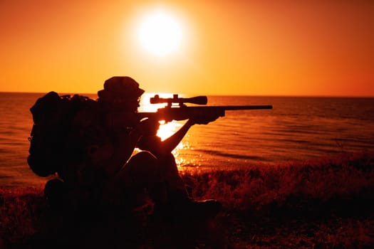 Commando team sniper, army special forces shooter aiming, shooting sniper rifle while sitting on sea or ocean shore during sunset. Coast or border guard soldier observing coastline with optical sight