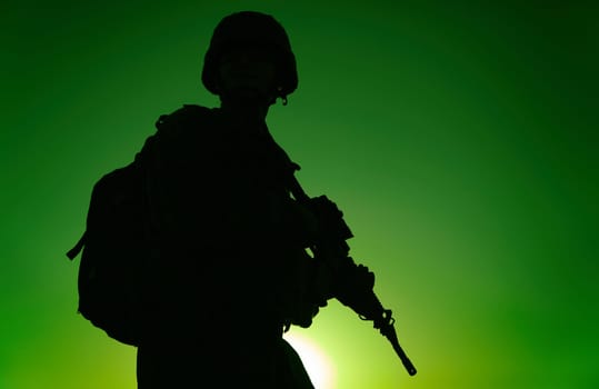 Silhouette of army rifleman in helmet and ammunition, carrying tactical backpack, walking with service rifle on background of sunset sky. Counter terrorist forces fighter marching at night mission