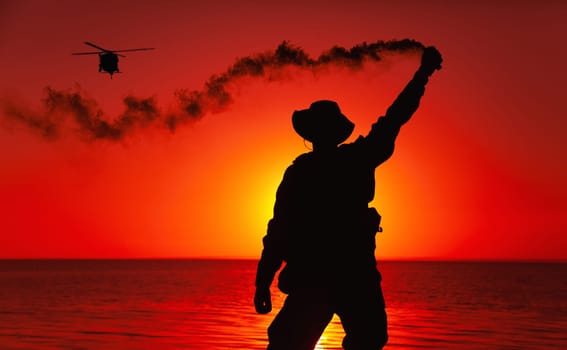 Silhouette of army special operations forces soldier, commando fighter signaling, marking landing spot or evacuation area for helicopter pilot with smoke flair while standing on shore during sunset