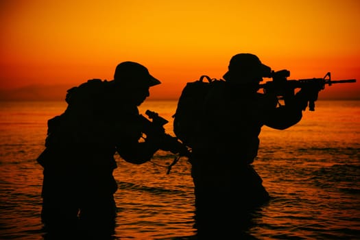 Army soldiers team, special operation forces infantrymen landing on seacoast, aiming and shooting with service rifle during firefight on shore at evening or morning time. Military amphibious operation