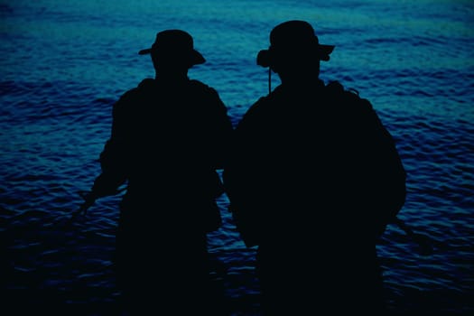 Two commando soldiers, army special operations fighters aiming assault rifles while coming out from water on shore at sunset or dawn. Coast guard shooters landing on sea coast, sneaking in water