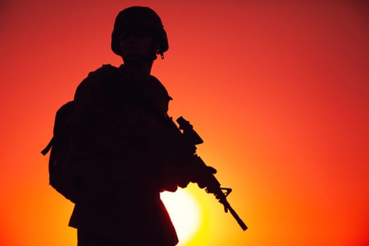 Silhouette of army special forces rifleman, Marines, coast guard or anti-terrorist squad soldier in ammunition and helmet, armed service rifle, standing on ocean shore, patrolling seacoast at sunset