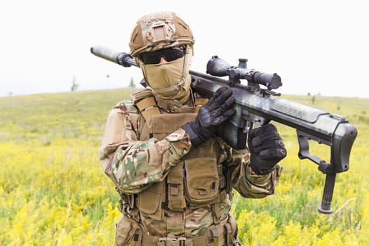 Special forces soldier walks across the yellow field with sniper rifle close up