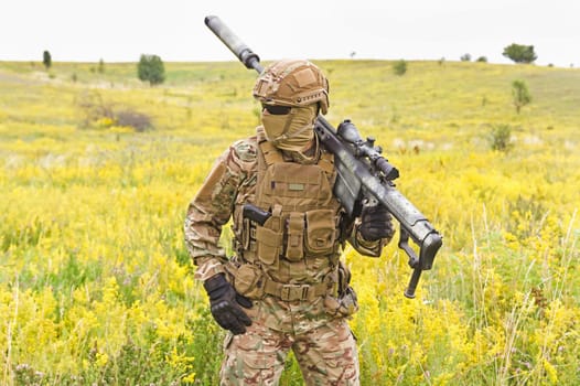 Soldier in a special military uniform, with a helmet on his head and with a sniper rifle in the field
