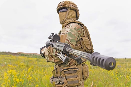 Special forces soldier standing in the green field with sniper rifle