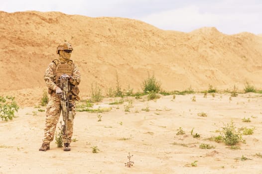 Equipped and armed special forces soldier, army ranger standing in the desert with copy space. Concept of military anti-terrorism operations, special operations of NATO forces.