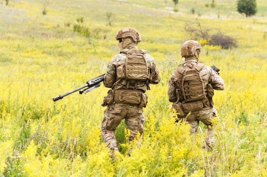 Two equipped and armed special forces soldiers with rifles in the blooming field