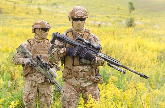 Two armed special forces soldiers with sniper rifles standing in the blooming field