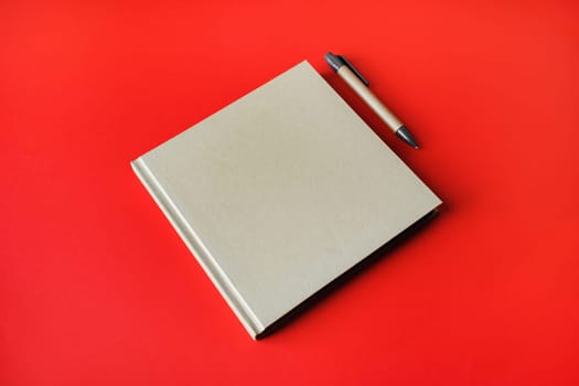 Photo of blank kraft closed brochure and pen on red paper background. Responsive design mockup. Template for placing your design.