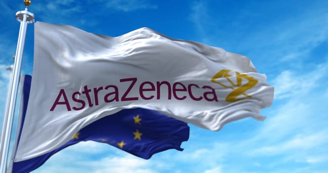Rome, Italy, January 28, 2021: White flag with the Astrazeneca logo waving in the wind with the European flag in the background. In early 2021 there were problems with the European Commission over the delivery of covid19 vaccine doses