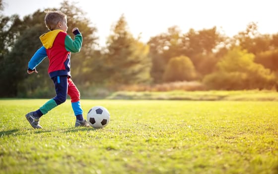 Child playing football on the field with gates. Active boy in summer with ball