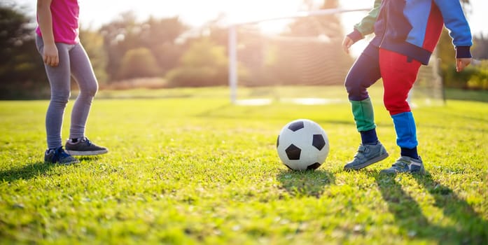 Children playing football on the field with gates. Active boy and girl in summer with ball