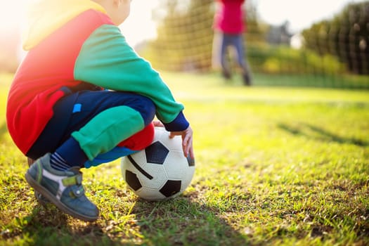 Children playing football on the field with gates. Active boy and girl in summer with ball
