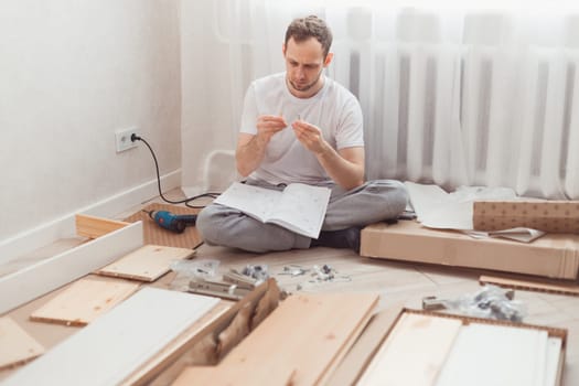 Man self-assemblies wooden furniture at home without master. Read instructions. Diy concept.