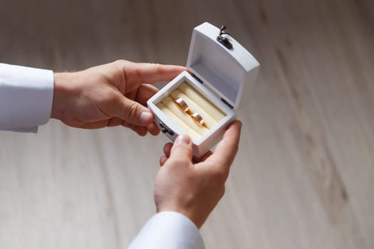 White wooden box with two gold wedding rings in groom hands, close up view, wedding accessories