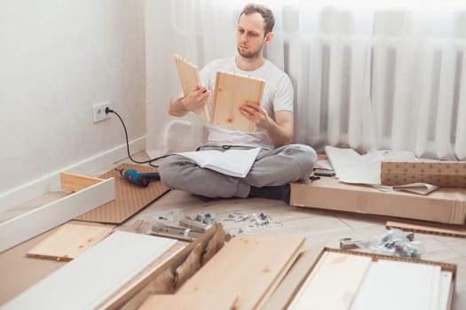 Man self-assemblies wooden furniture at home without master. Read instructions. Man reading instructions. Diy concept