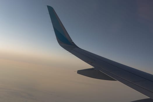 In the air, view of the airplane wing with horizon of dark blue sky and clouds background in sunrise time, viewed from the airplane window