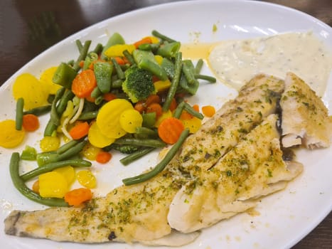 To portions of fresh grilled pollock or coalfish served with colorful salad and slices of lemon, close up high angle view