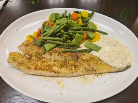 To portions of fresh grilled pollock or coalfish served with colorful salad and slices of lemon, close up high angle view