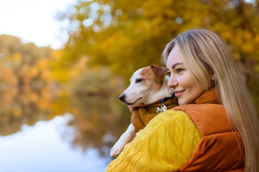 Portrait of a smiling young woman kissing a dog in a field. Dog lover stylish girl hugging her dog while walking. Animal friendship concept.