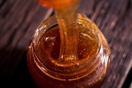 Honey dripping from a wooden honey dipper   on black background