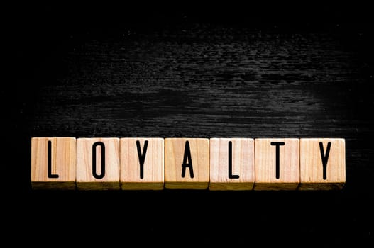 Word Loyalty.Wooden small cubes with letters isolated on black background.Concept image.