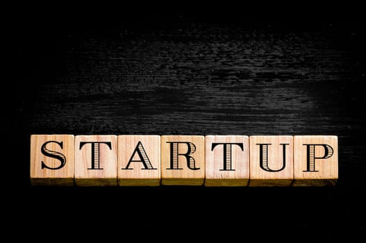 Word Startup. Wooden small cubes with letters isolated on black background.Concept image.