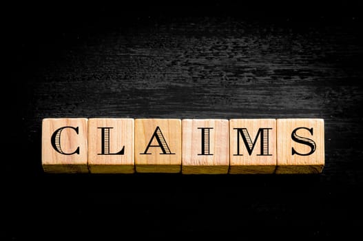 Word Claims. Wooden small cubes with letters isolated on black background.Concept image.