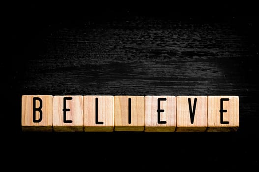 Word Believe. Wooden small cubes with letters isolated on black background.Concept image.