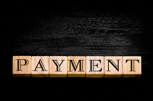 Word Payment.Wooden small cubes with letters isolated on black background.Concept image.