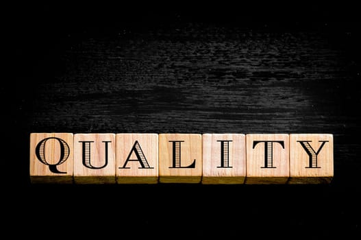 Word Quality.Wooden small cubes with letters isolated on black background.Concept image.