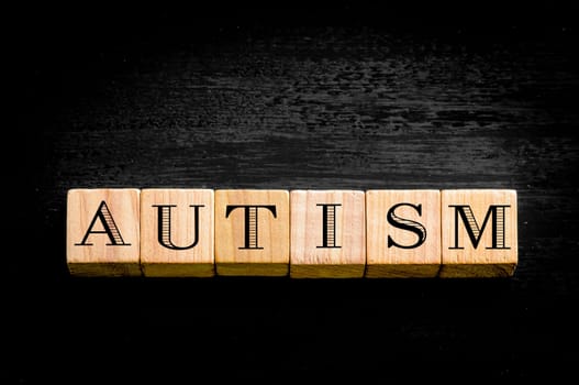 Word Autism. Wooden small cubes with letters isolated on black background.Concept image.