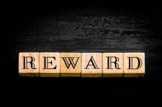 Word Reward. Wooden small cubes with letters isolated on black background.Concept image.