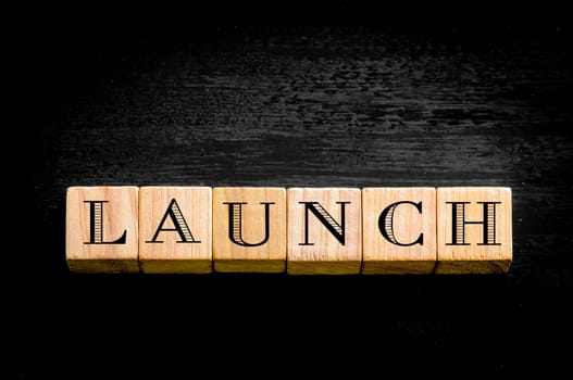Word Launch. Wooden small cubes with letters isolated on black background.Concept image.